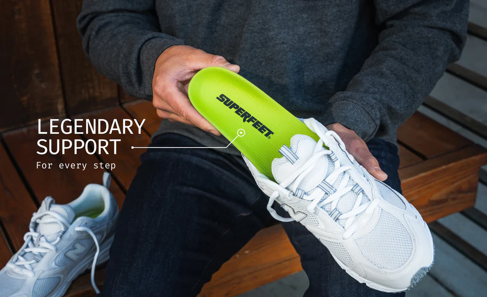 View2_All-Purpose_Support_High-Arch_2731x1667_2484dff4-cf84-44fd-9a7c-5b1b9d8d816a - Horizon Industries Person holds a lime-green Superfeet insole beside a white athletic shoe, highlighting supportive footwear.”