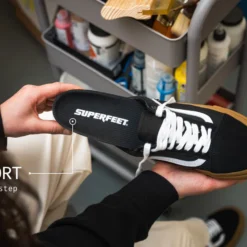 Close-up of a black Superfeet sneaker being held, with a 'Thin Support' annotation and 'For every step' text in a workshop setting
