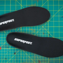 View8_All-Purpose_Support_Low-Arch_2731x1667_6633671d-3e14-40da-835f-e2709dbfa653 - Horizon Industries Two black Superfeet insoles lying on a teal grid cutting mat with yellow lines, logo visible on each insole.