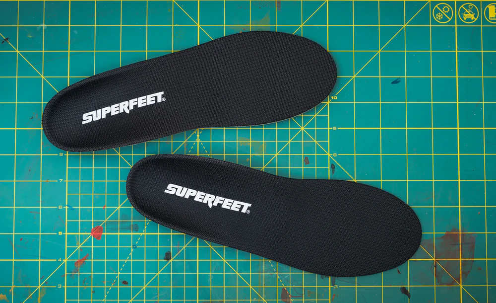 View8_All-Purpose_Support_Low-Arch_2731x1667_6633671d-3e14-40da-835f-e2709dbfa653 - Horizon Industries Two black Superfeet insoles lying on a teal grid cutting mat with yellow lines, logo visible on each insole.