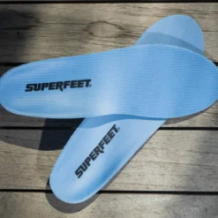 View8_All-Purpose_Support_Medium-Arch_2731x1667_420e7a4e-0ad6-48b2-a51d-6fa8b13fa45b - Horizon Industries Light blue Superfeet shoe insoles laid crossing on a wooden bench surface.